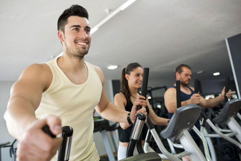 38497815 active people at gym in elliptical bike, smiling man in focus.